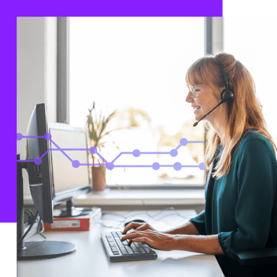 Photo of a smiling female contact center agent, seen from the side. She is typing on her keyboard while talking to a customer through her headset.