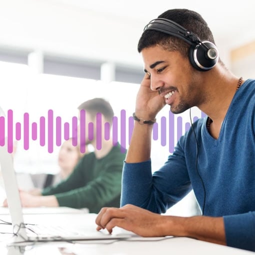 Image of a man wearing a headset and looking at a laptop while working in an office.