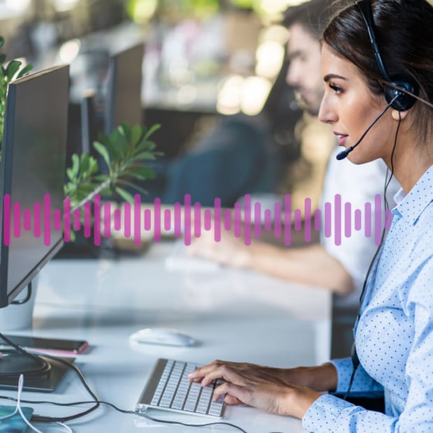 Photo of a call center agent typing data into her computer while taking to a customer on her phone headset. A small row of purple "sound waves" run across the frame representing communication.