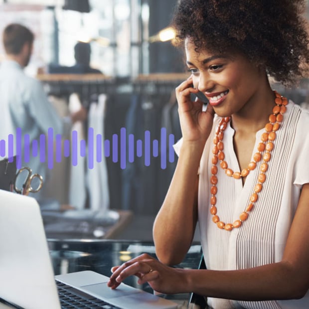 Photo of a smiling employee in a store. She is talking on the phone while scrolling on her computer. In the background, a series of small purple vertical lines run across the frame, representing communication.
