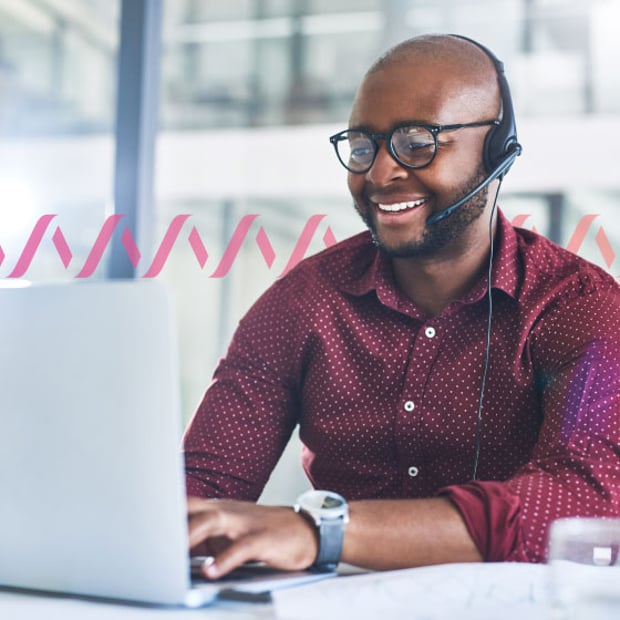 Photo of a smiling employee talking to a customer on his headset while typing on his laptop. In the background, a series of small pink gradient wave lines run across the frame, representing communication
