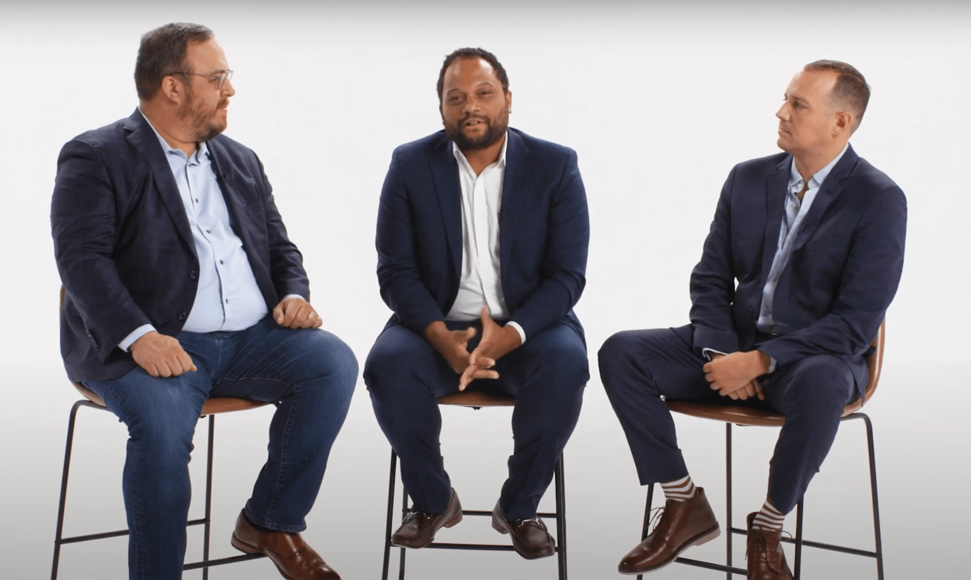 Video frame showing three men on stools.